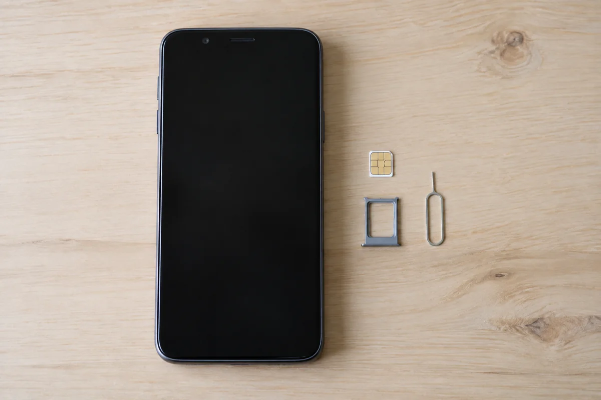 A generic phone beside a SIM tray, unmarked SIM card and eject tool